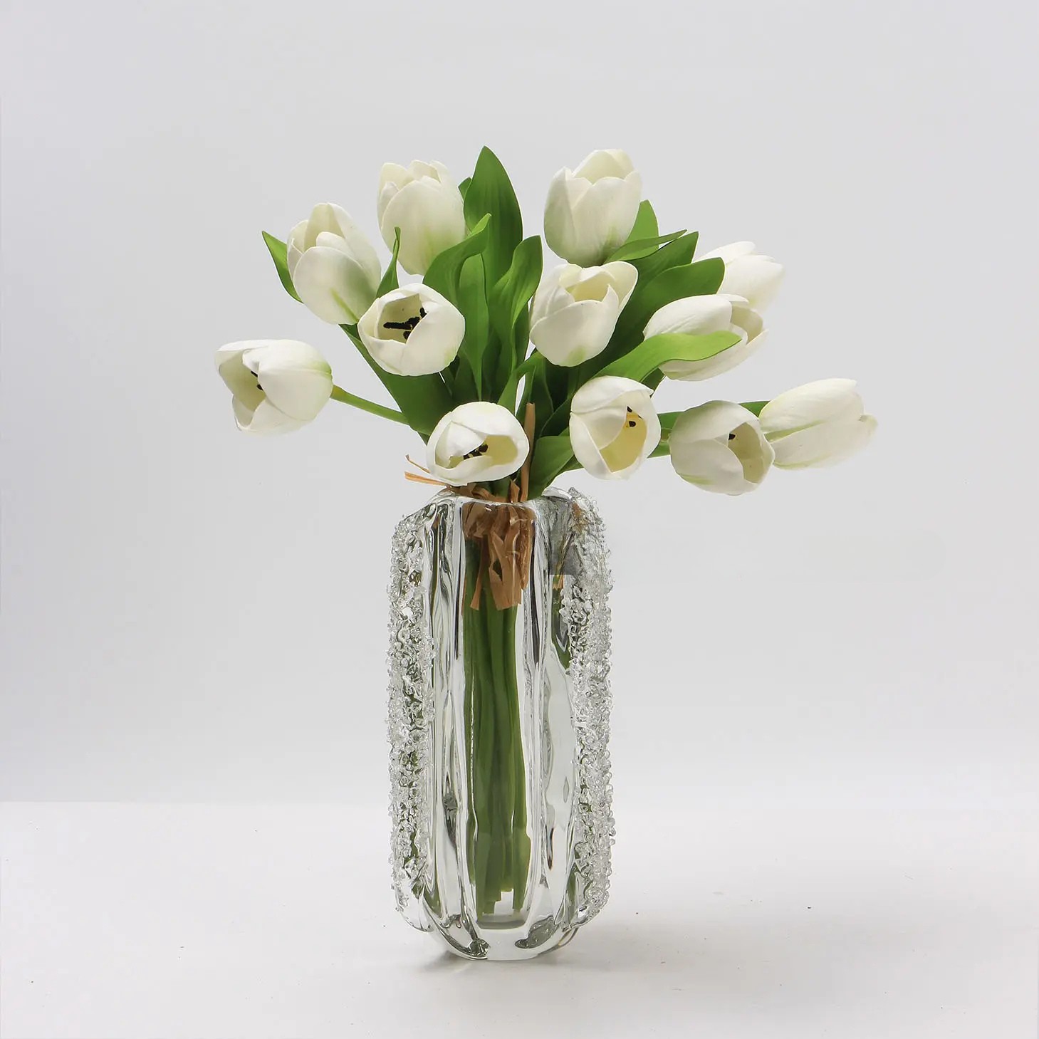 Vază decorativă din sticlă transparentă cu detalii texturate, umplută cu lalele albe