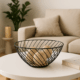 Coș decorativ din metal negru cu design geometric, plasat pe o masă albă de cafea într-un living modern, conținând bile decorative din sfoară.