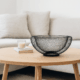 Coș decorativ din metal negru pe o masă de cafea din lemn într-un living modern.